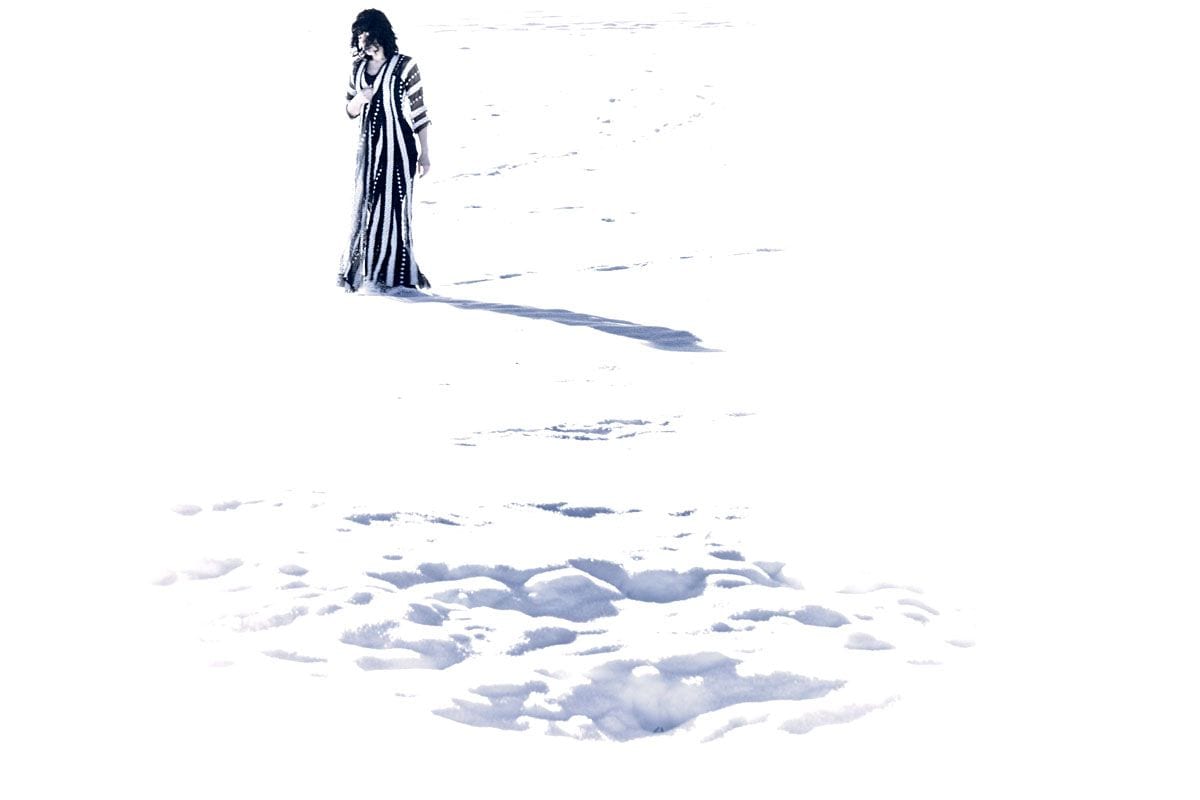 A lone robed figure stands in a vast field of snow, dwarfed by white emptiness — Baghdadi Mem/Wars, Absence/Presence